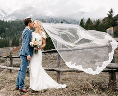 a bride and groom kissing in front of a mountain view with their veil blowing in the wind