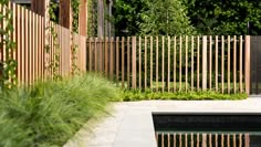 a wooden fence next to a pool surrounded by greenery