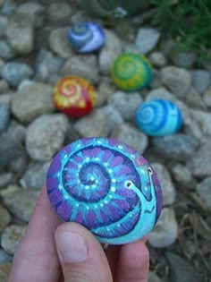 a hand is holding a painted rock in front of some rocks and stones with different designs on it