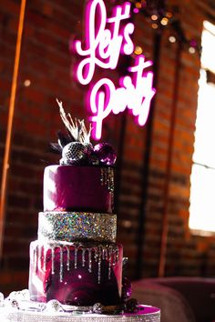 a three tiered cake sitting on top of a table next to a neon sign