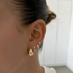 a close up of a person's ear wearing gold earrings with small drops on them