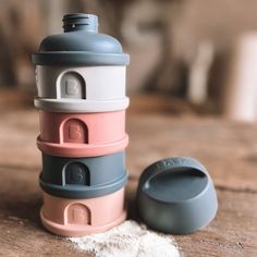 a stack of different colored containers sitting on top of a wooden table next to a salt shaker