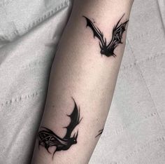 a black and white photo of a bat tattoo on the left arm, with two bats flying above it