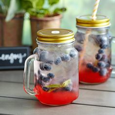 two mason jars filled with blueberries sitting on a table next to potted plants