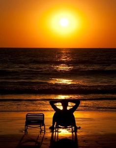 a person sitting in a chair on the beach at sunset