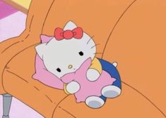 a hello kitty sitting on top of an orange couch with a pink bow around it's neck