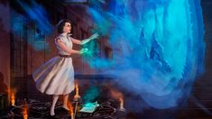 a painting of a woman in white dress standing next to a giant blue object with flames coming out of it