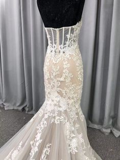 the back of a wedding dress on display in front of a gray curtained background