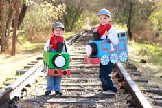 two children are standing on the railroad tracks with their train costumes made to look like trains