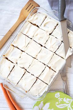 carrot cake with white frosting in a glass dish next to utensils and spoons