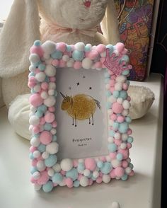 a white stuffed animal sitting next to a pink and blue frame