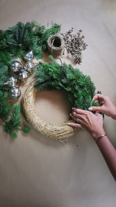 a woman is decorating a wreath with silver balls and greenery on the table