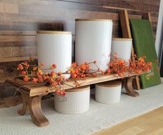 three white vases sitting on top of a wooden bench next to flowers and plants