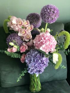 a vase filled with lots of purple and pink flowers on top of a green couch