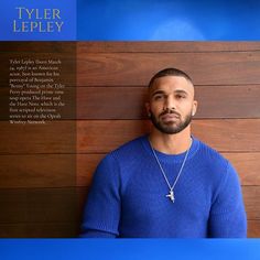 a man wearing a blue sweater is standing in front of a wooden wall with the words tyler lepley on it