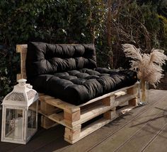 a couch made out of wooden pallets sitting on top of a deck next to a lantern