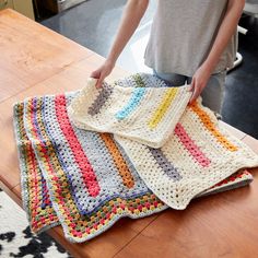 a person standing over a wooden table with a crocheted blanket on it