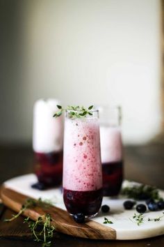 two glasses filled with liquid sitting on top of a white plate next to blueberries