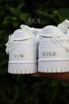 a pair of white shoes with flowers on the front and side are held in someone's hand