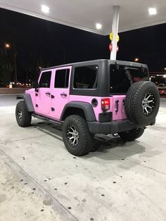 a pink and black jeep is parked in a parking lot at night with its lights on