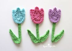 three crocheted tulips sitting side by side on a white surface, one is pink, the other is blue