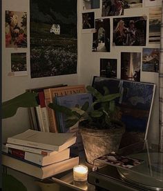 a desk with books, plants and pictures on the wall above it is lit by a candle