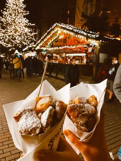 a person holding up two pastries in front of a christmas tree on the street