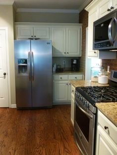 a stainless steel refrigerator and stove in a kitchen with white cabinets, wood flooring and granite counter tops