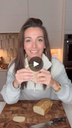 a woman sitting at a kitchen table with bread on the cutting board and knife in front of her