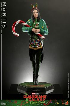 a statue of a woman dressed in green and red holding a candy cane on top of a book