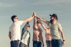 group of young men holding their hands high in the air while standing on top of a hill