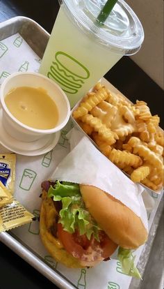 a tray with a sandwich, fries and drink on it next to a cup of coffee