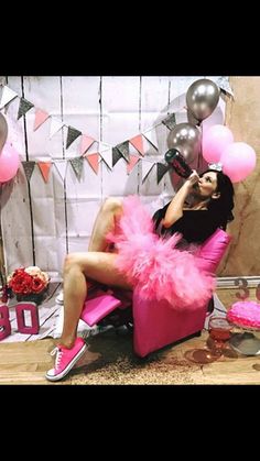 a woman sitting in a chair with pink feathers on her feet and balloons around her