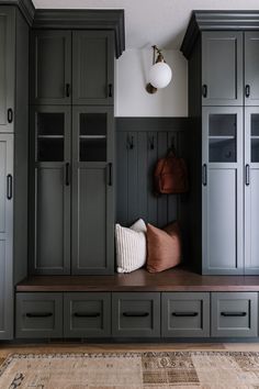 a bench in the middle of a room filled with gray cabinets and pillows on top of it