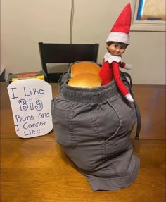 an elf sitting in a bag on top of a wooden table next to a sign that says i like big buns and don't look like