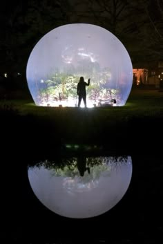 a man standing in front of a large white ball at night with lights on it