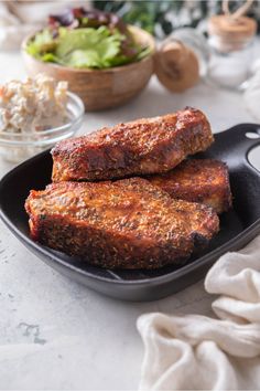 two pieces of meat sitting in a pan on a table next to a bowl of salad