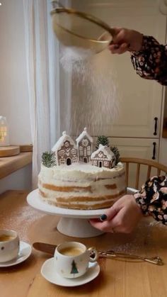 a woman is sprinkling icing onto a cake on a table with cups and saucers