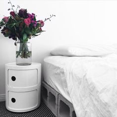 a vase filled with flowers sitting on top of a white dresser next to a bed