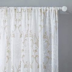 a white curtain hanging on the side of a window with gold and white floral designs