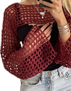 a woman is wearing a red crochet sweater and holding a cell phone in her hand