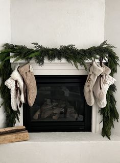 stockings hanging from a mantel over a fireplace with evergreen garland on the mantles