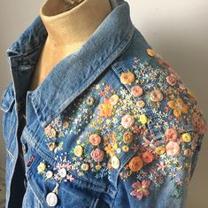 a woman's jean jacket with colorful flowers on the back and buttons at the front