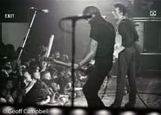 two men standing on stage with microphones in front of them and an audience behind them