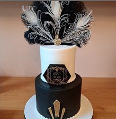 a three tiered black and white cake with feathers on it's top layer