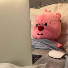 a pink stuffed animal with glasses is sitting in front of a laptop computer on a bed