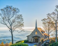 an old church on top of a hill with trees in the foreground and mountains in the background