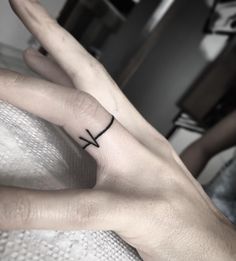 a person's hand with a small cross tattoo on the middle finger and an arrow in the middle