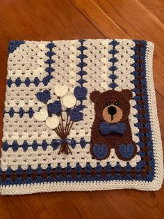 a crocheted blanket with a teddy bear and flowers on the bottom, sitting on a wooden floor