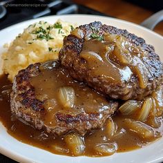 two meat patties covered in gravy on a plate with mashed potatoes